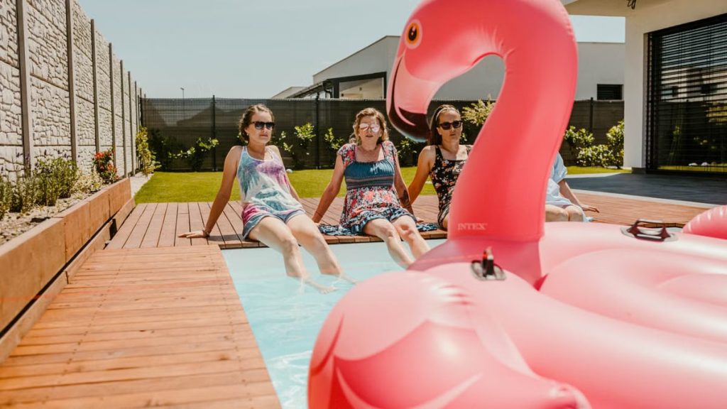 Women enjoying a sunny day by the pool with an inflatable flamingo, epitomizing summer fun.