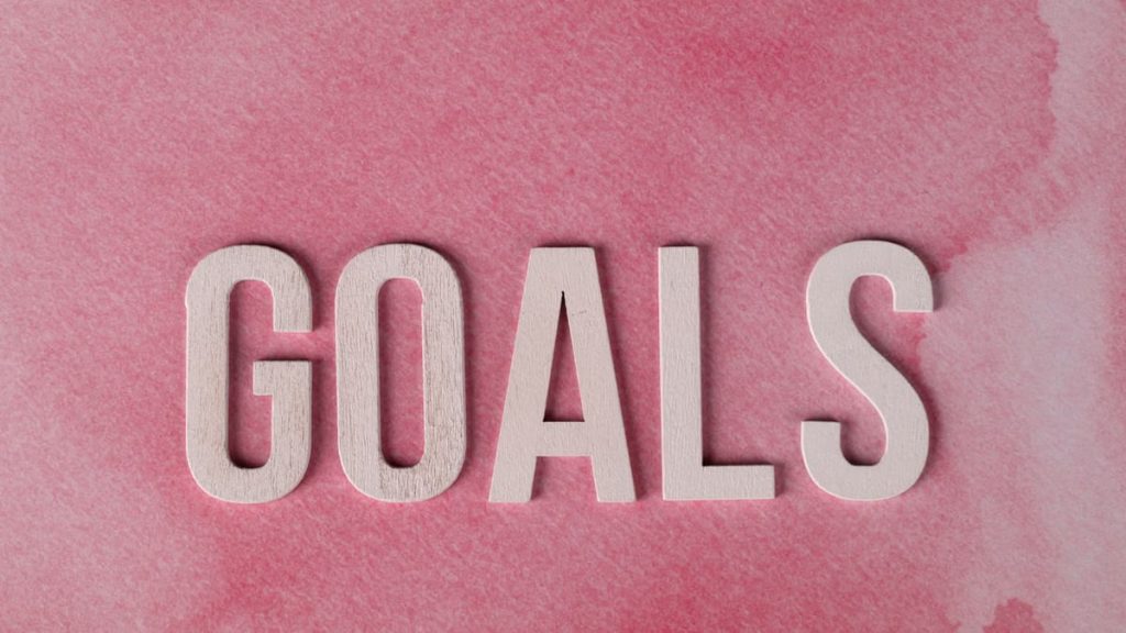Motivational word 'GOALS' on a pink watercolor background for inspiration.